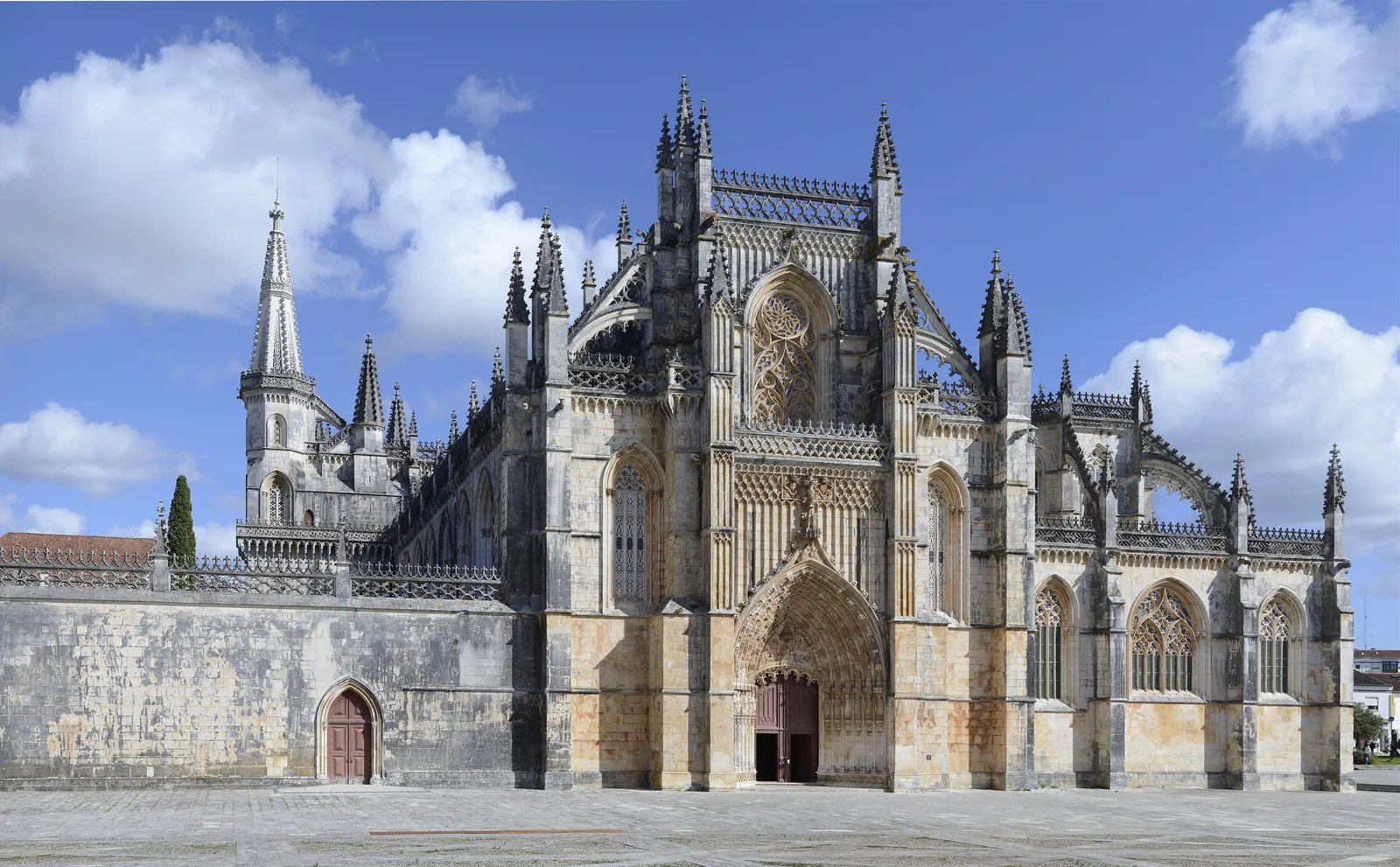 The Gothic west façade and main portal of the Monastery of Batalha, with pinnacles and tracery, under a blue sky