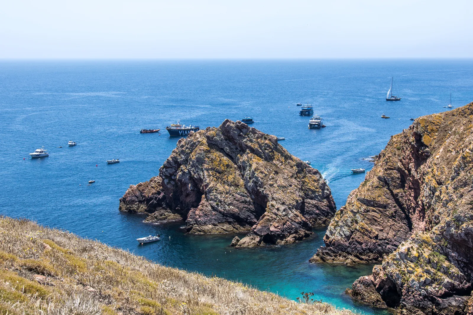Rugged granite rocks and a turquoise cove off Berlenga Grande, with boats anchored in the deep blue Atlantic