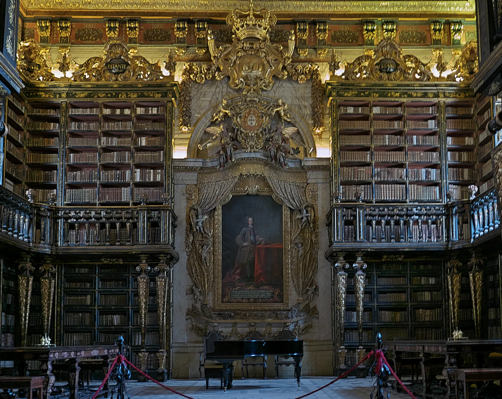 Gilded baroque interior of the Biblioteca Joanina, with carved wooden bookcases and the portrait of King João V