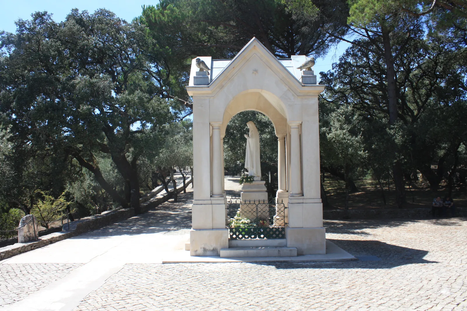 The white stone monument marking the fourth apparition at Valinhos, framed by holm oaks on a sunny day