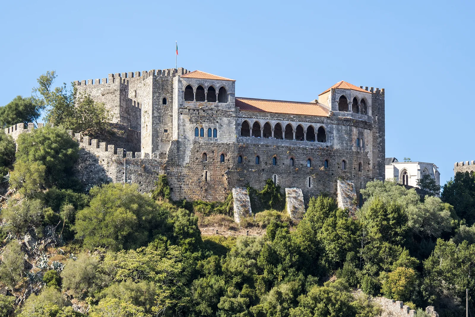 Leiria Castle with its arcaded royal palace loggia rising above green wooded slopes against a blue sky