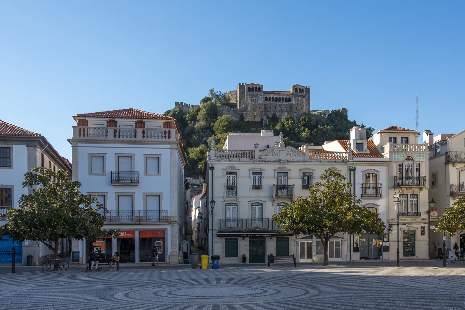 Praça Rodrigues Lobo in Leiria's historic centre, its patterned cobbles and pastel townhouses beneath the castle on the hill