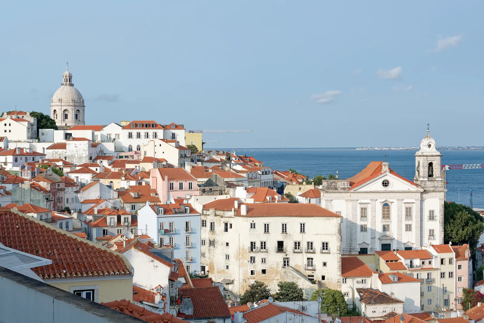 Terracotta rooftops of Alfama seen from the Miradouro de Santa Luzia, with the dome of the National Pantheon, the bell tower of Santo Estêvão and the Tagus beyond