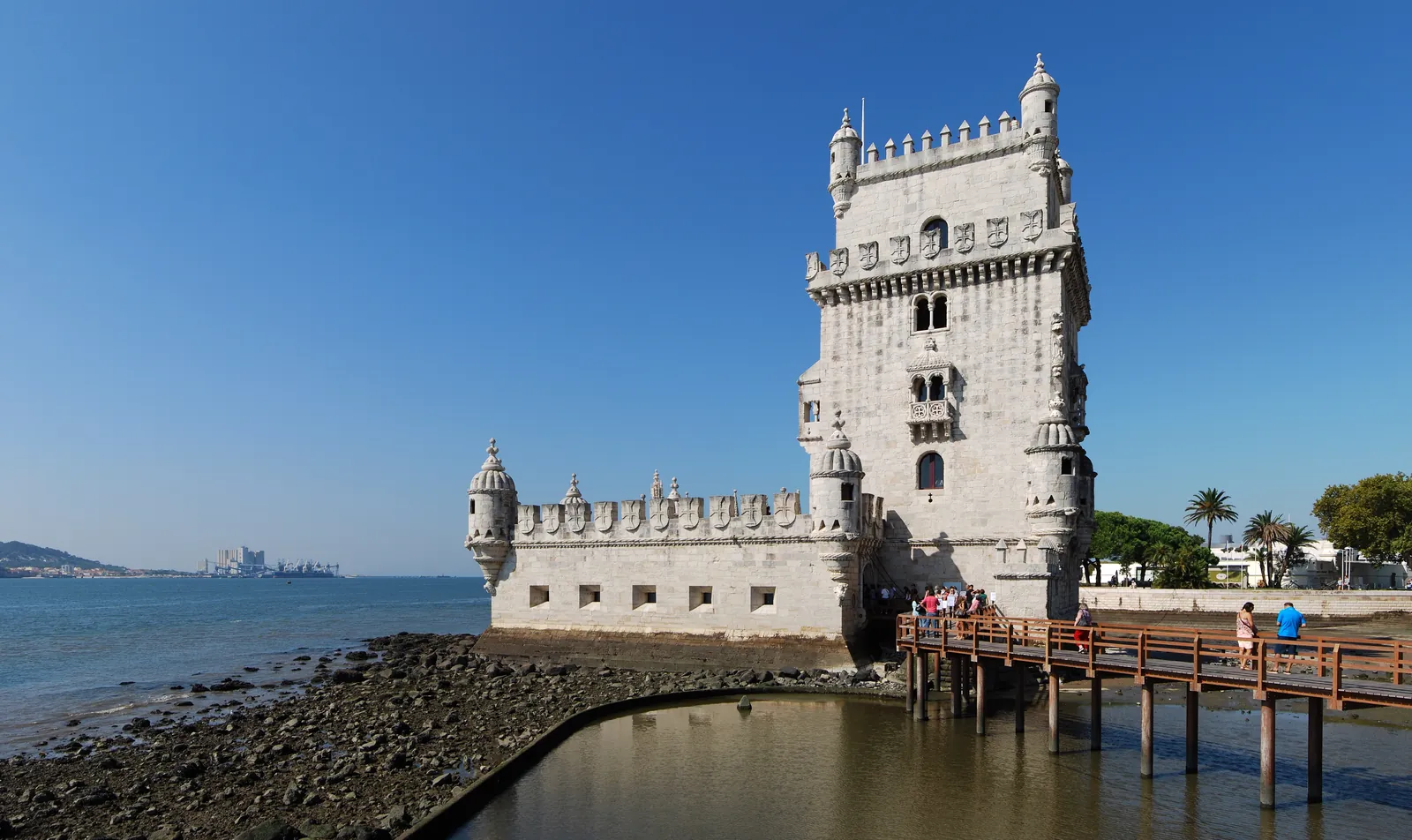 The Manueline Belém Tower rising from the Tagus shore in Lisbon, reached by a wooden footbridge, under a clear blue sky