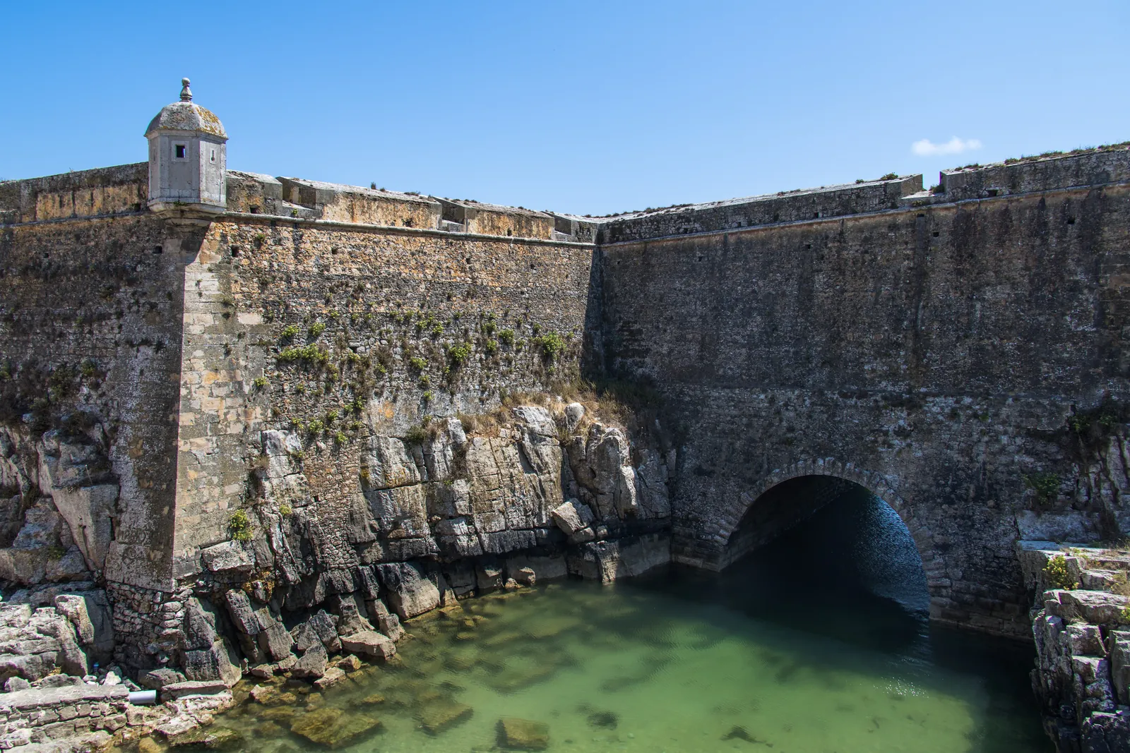 Stone bastion and sentry box of the Peniche Fortress rising from rocks above clear green seawater