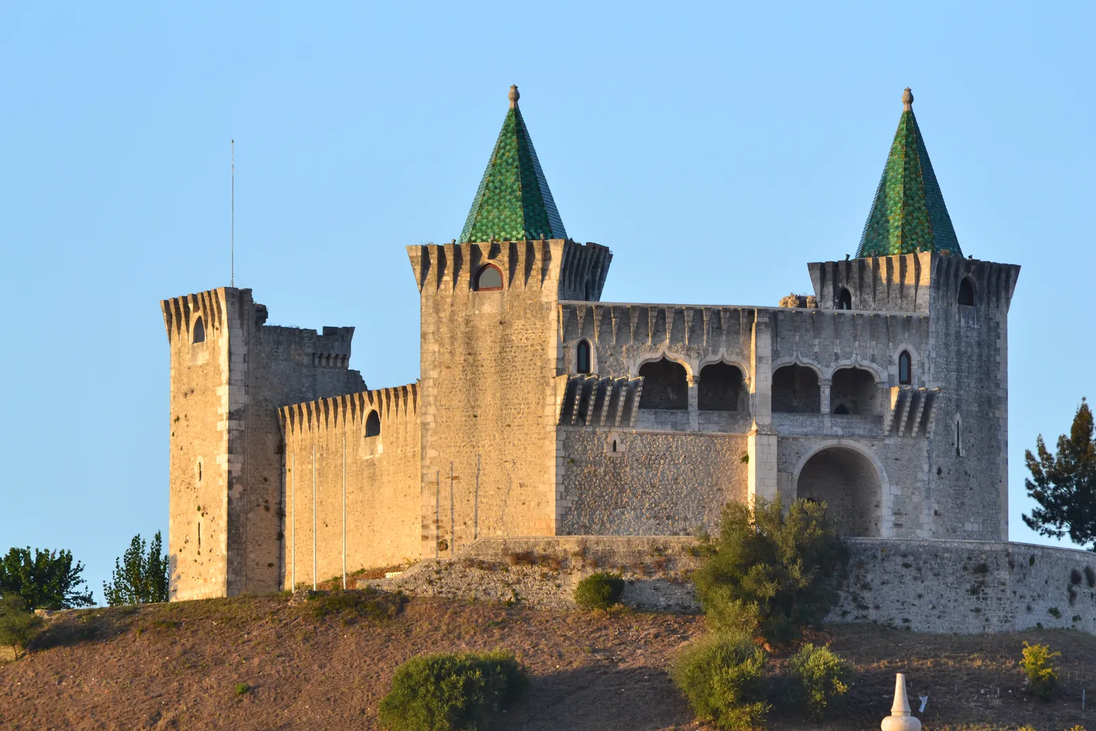 Porto de Mós Castle with its two green-tiled conical towers and Gothic loggia glowing in late afternoon sun