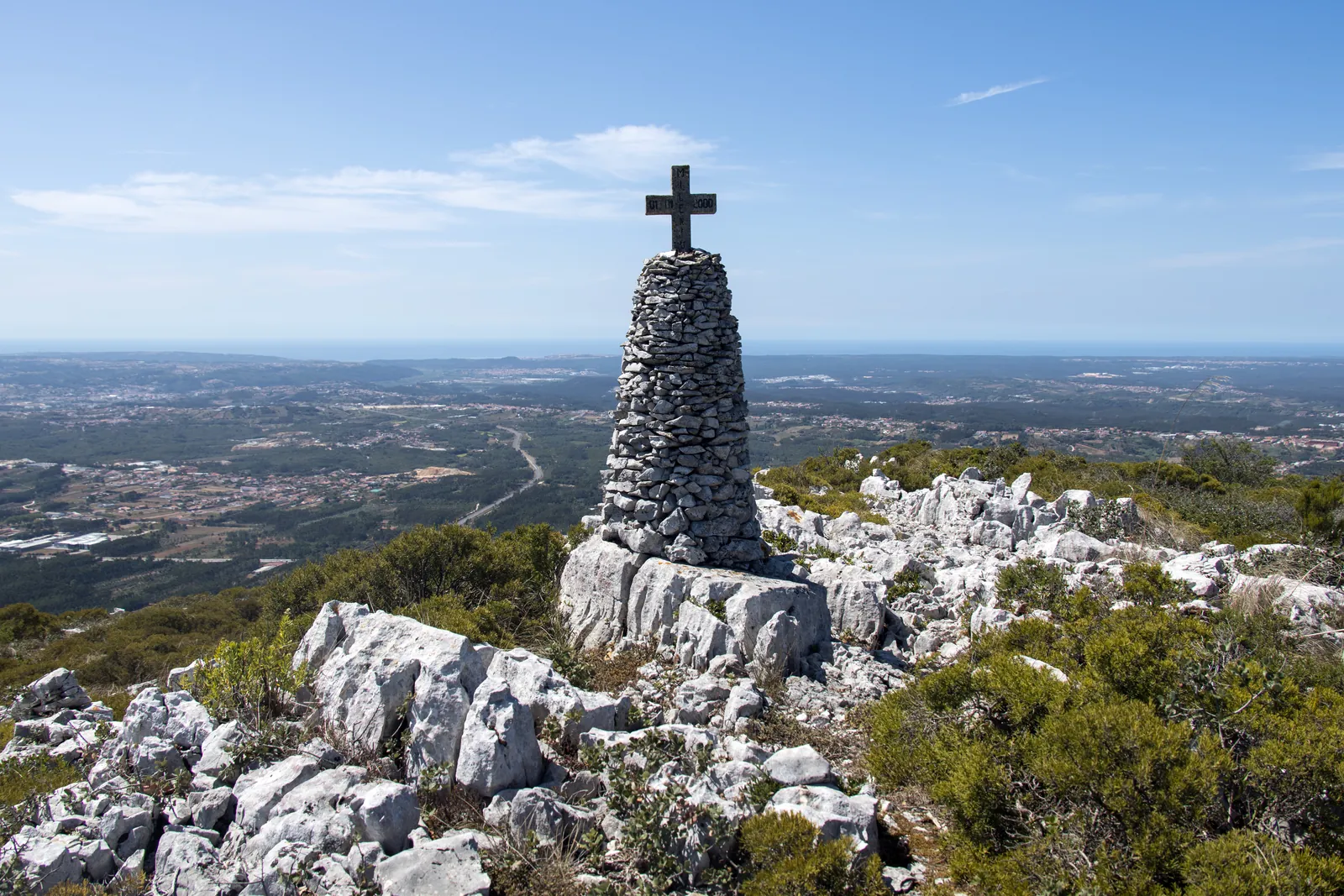 White limestone outcrops and a stone cairn with a cross on the Serra dos Candeeiros, overlooking the plain