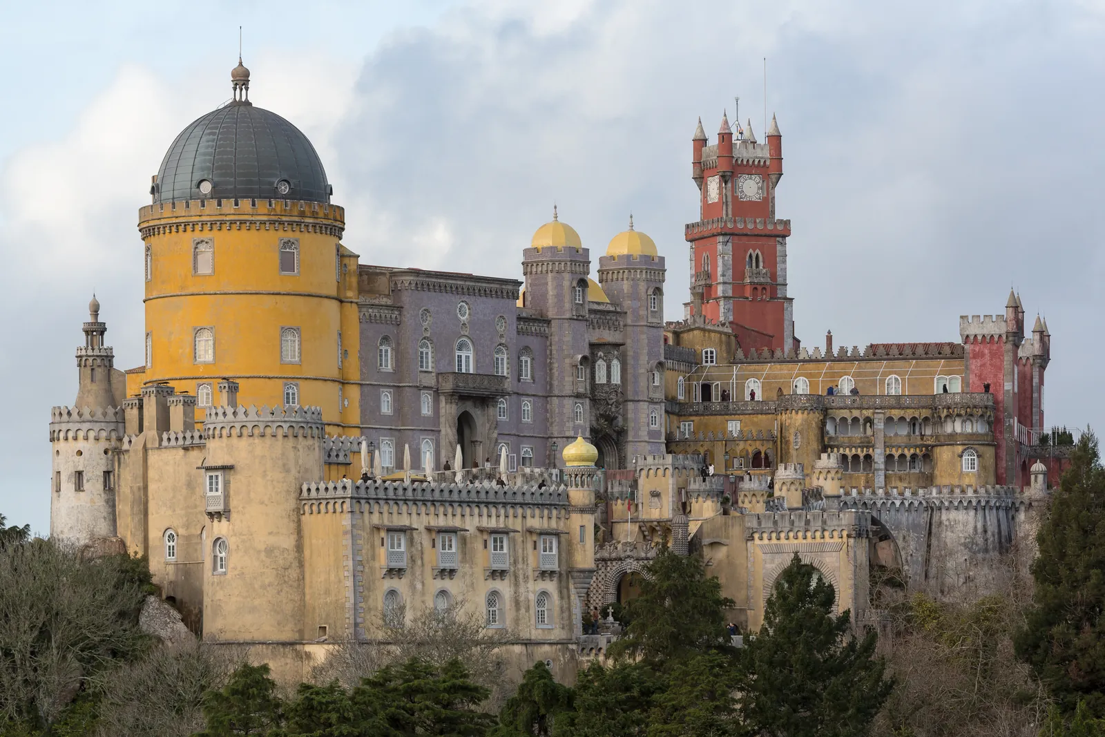 The ochre, lilac and red towers and domes of Pena Palace rising above the wooded hills of Sintra
