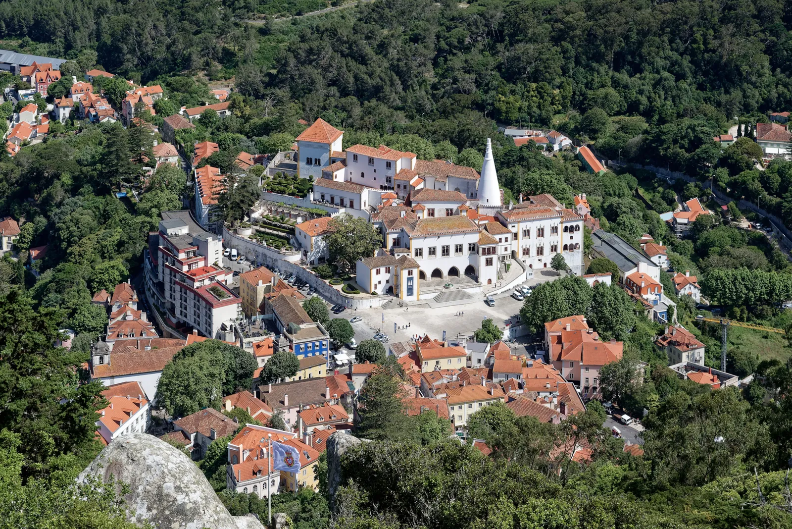 Sintra's historic centre seen from the Moorish Castle, the white National Palace with its two conical chimneys amid terracotta roofs and green hills